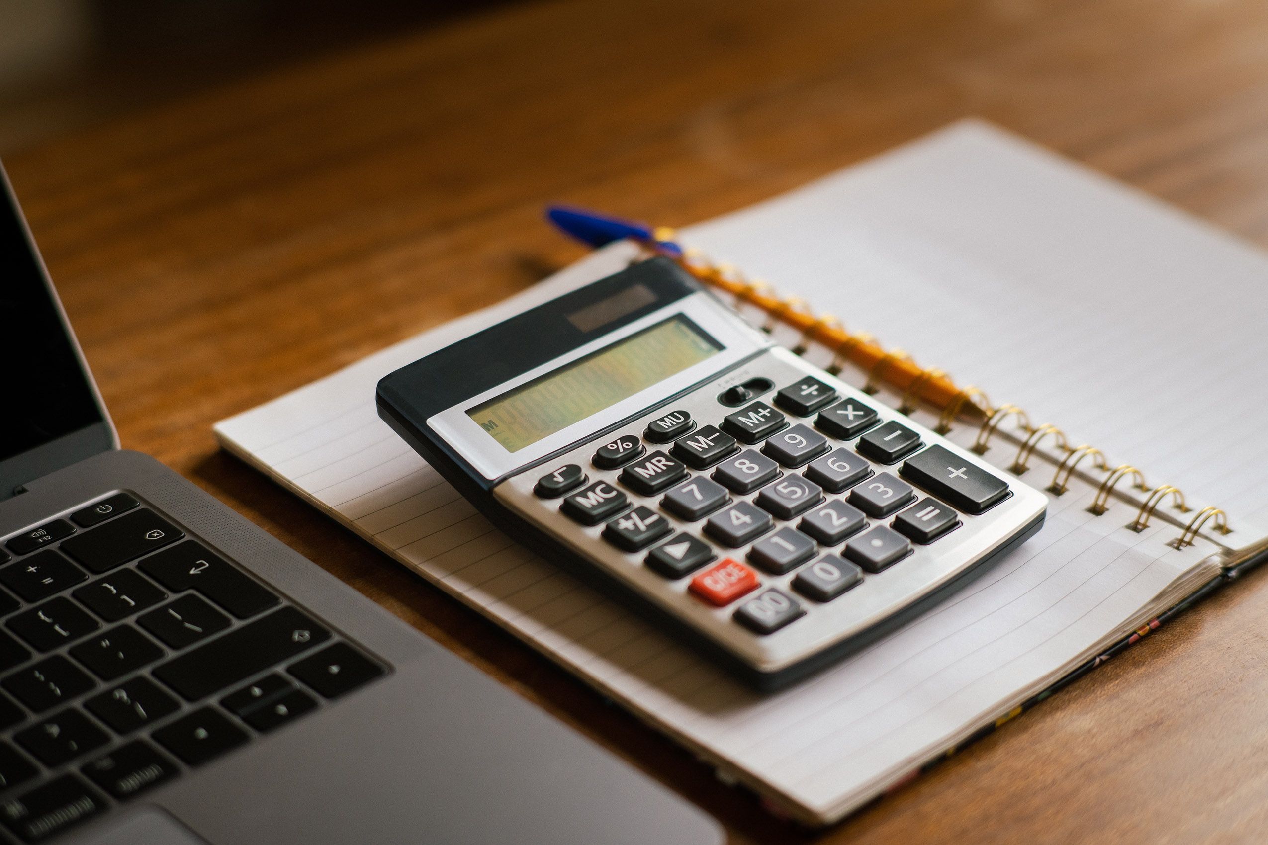 Calculadora, laptop e óculos sobre mesa, representando o cálculo de custo entre planilha e sistema para eventos