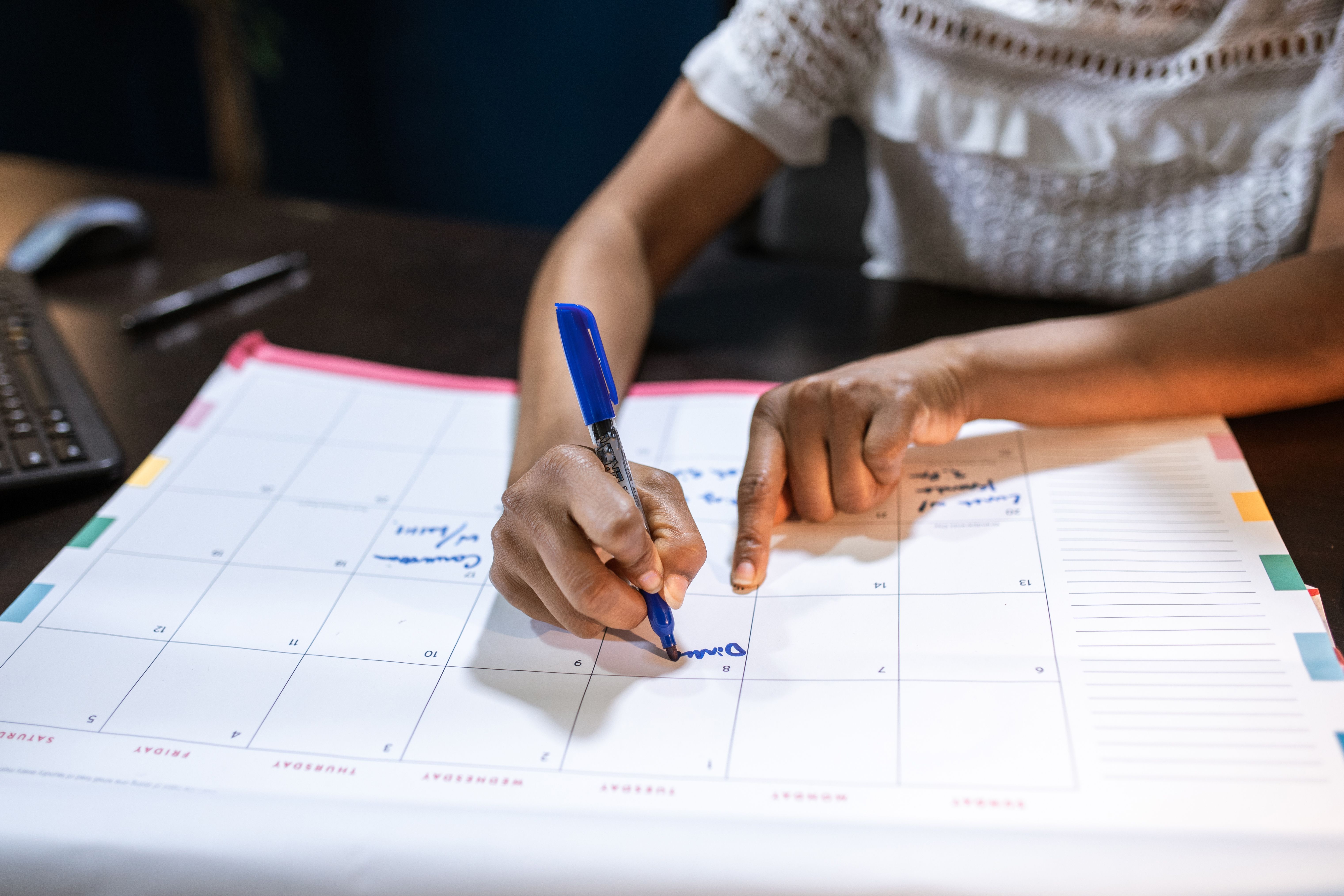Mulher marcando datas importantes em um calendário de mesa, planejando a agenda de eventos