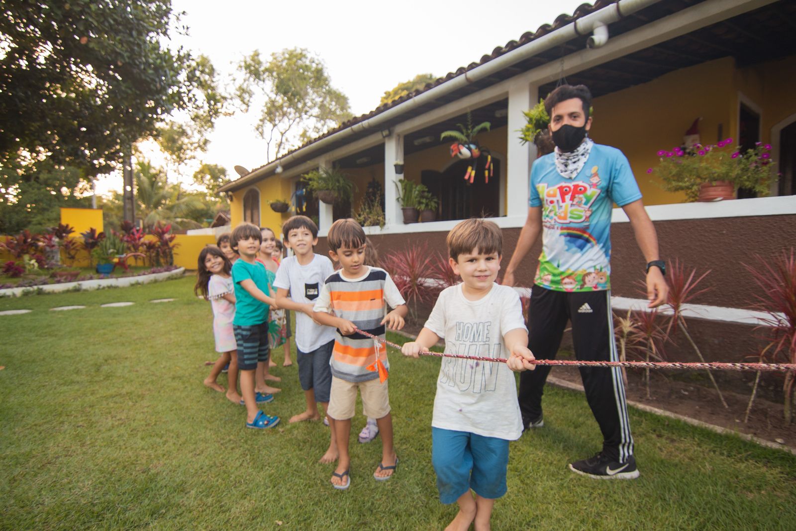 Recreador conduz brincadeira de cabo de guerra com crianças em festa infantil ao ar livre